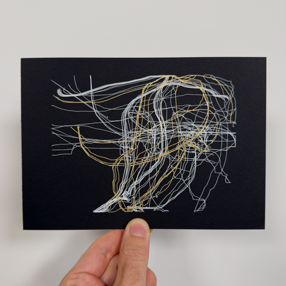 Hand holding a black card with white and gold string art design on a light gray background